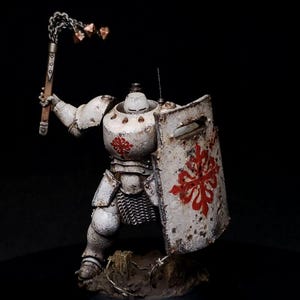 Puede incluir: Una figura de robot blanca y desgastada, que lleva una armadura y sostiene un arma de cadena con púas y un escudo con un diseño de cruz roja.