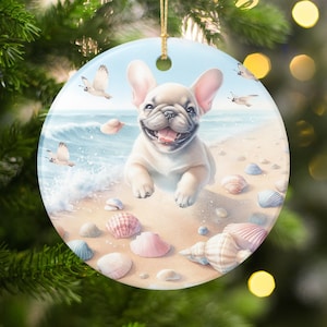 May include: Round ceramic Christmas ornament featuring a happy French Bulldog on a beach with seashells and seagulls. The background shows the ocean and a blue sky. The ornament has a gold string for hanging.