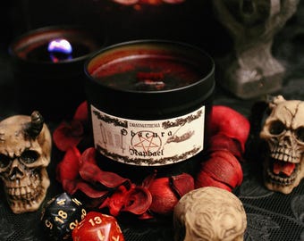 May include: A black candle jar with a red wax interior and a label that reads "Draumathema Obscura Raphael". The candle is surrounded by red rose petals and three small skull figurines. Two red and black dice are also in the image.