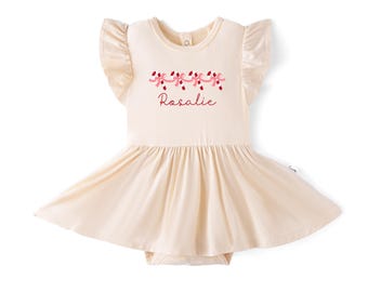May include: A cream-colored short-sleeve dress with ruffled shoulders and a flared skirt. The chest features a graphic of four candy canes tied with pink ribbons and the name Rosalie printed in a dark red script font below the graphic.