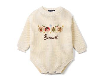 May include: A cream-colored long-sleeve knit romper featuring a ribbed texture and a crew neckline. The chest displays embroidered holiday icons including a reindeer, snowman, Christmas tree, and gingerbread man, with the name Bennett below.