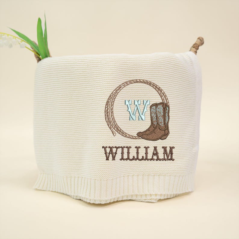 Puede incluir: Manta de punto color crema con un dise&ntilde;o bordado que presenta una bota de vaquero, la letra "W" y el nombre "WILLIAM". El dise&ntilde;o est&aacute; enmarcado por un c&iacute;rculo de cuerda. La manta tiene un borde acanalado.