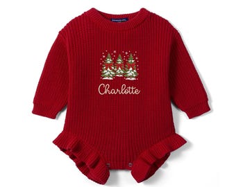 May include: A long-sleeve red knit baby romper featuring a ribbed texture, a crew neckline, and ruffled leg openings. The chest displays an embroidered graphic of three snow-covered pine trees with red bows and the name Charlotte in white script.