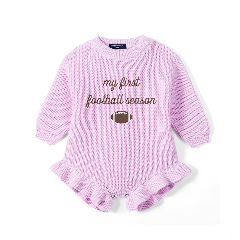 May include: A light purple long-sleeve knit romper featuring a ribbed crew neckline and cuffs. The chest displays the brown text 'my first football season' above a brown football graphic. The bottom hem is finished with a ruffled knit trim.