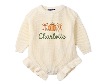 May include: A cream-colored long-sleeve knit romper featuring a ribbed texture and ruffled leg openings. The chest displays an embroidered orange pumpkin flanked by two tan bows, with the name Charlotte stitched in dark green cursive script below.