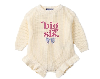 May include: A cream-colored long-sleeve knit romper featuring a ribbed texture, a round neckline, and ruffled leg openings. The front displays the pink text 'big sis.' above a small, detailed illustration of a blue and pink striped bow.