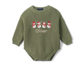 May include: An olive green long-sleeve knit romper featuring an embroidered row of four snowmen wearing red hats and scarves, with the name Oliver stitched in beige thread below the snowmen and a Swaddle A.M. label at the neckline.
