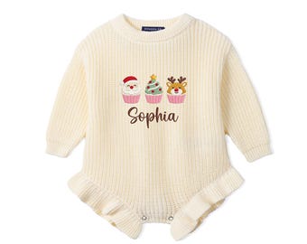 May include: A cream-colored long-sleeve knit romper featuring a ruffled hem and an embroidered graphic of three holiday-themed cupcakes, including Santa, a Christmas tree, and a reindeer, with the name Sophia embroidered in brown script below.