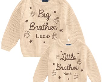 May include: Two cream-colored knit sweaters. The larger sweater says "Big Brother Lucas" with teddy bear and star accents. The smaller sweater says "Little Brother Noah" with similar details.