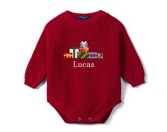 May include: A long-sleeved, deep red knit romper featuring a ribbed texture and a crew neckline. The center displays an embroidered graphic of stacked colorful gift boxes with bows, positioned above the white embroidered name Lucas.