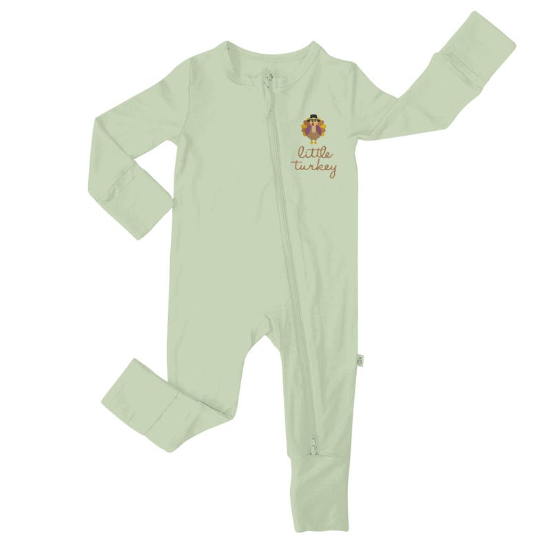 May include: Light green baby one-piece pajama with a full-length zipper. The pajama features a cartoon turkey graphic with the words "little turkey" in brown script. The long-sleeved pajama has ribbed cuffs at the wrists and ankles.