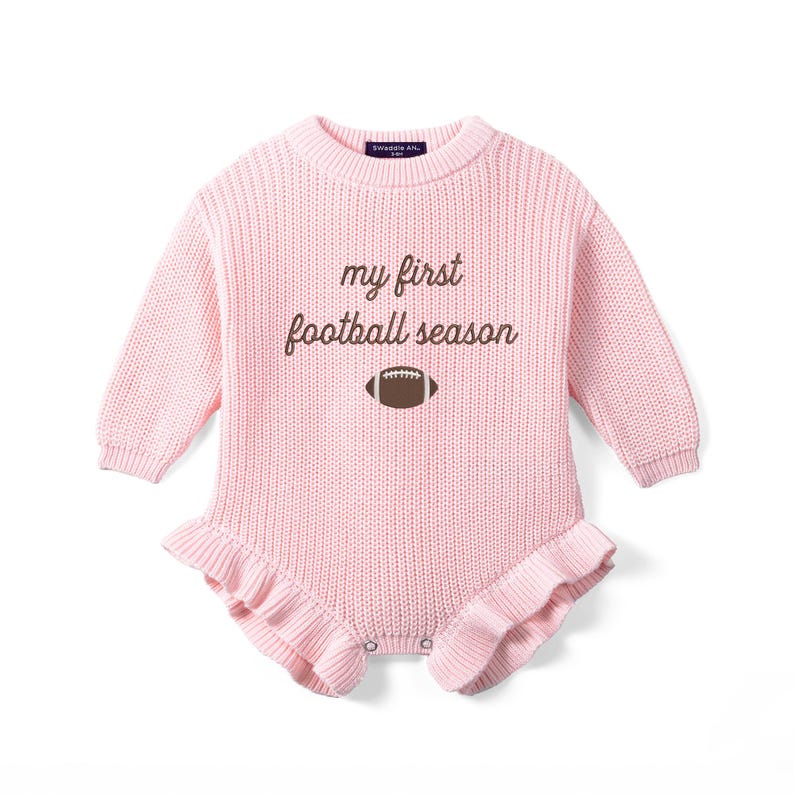 May include: A light pink long-sleeve knit romper featuring a crew neckline and ruffled leg openings. The chest displays the brown embroidered text "my first football season" above a small brown and white football graphic icon.