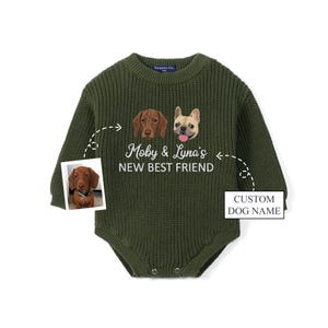 May include: An olive green long-sleeve knit romper featuring a graphic of two dogs and the white text Moby & Luna's NEW BEST FRIEND. A small inset photo shows a brown dachshund, and a box with an arrow points to the text CUSTOM DOG NAME.