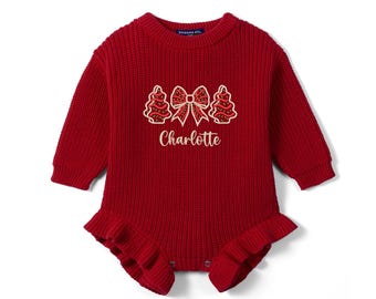 May include: A long-sleeved, deep red knit romper featuring a ribbed texture, a crew neckline, and ruffled leg openings. The chest displays an embroidered design of two Christmas trees flanking a central bow, with the name Charlotte below.