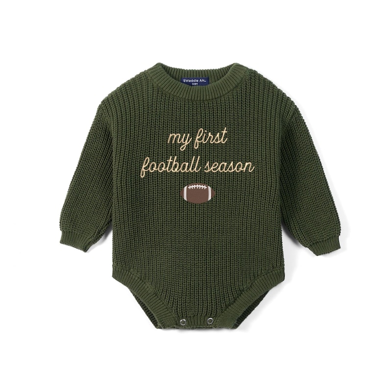 May include: An olive green long-sleeve knit romper featuring a crew neckline and ribbed texture. The chest displays the embroidered text "my first football season" in a light tan script font, positioned above a brown and white football graphic.