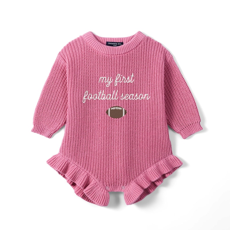 May include: A long-sleeved, pink knitted romper featuring a ribbed crew neckline and cuffs. The chest displays the white embroidered text 'my first football season' above a brown and white football graphic. The leg openings have ruffled edges.
