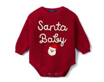Puede incluir: Un body de punto de color rojo oscuro para bebé con mangas largas, que presenta el texto bordado en blanco Santa Baby y una pequeña aplicación detallada de una cara de Papá Noel debajo de las letras. La prenda tiene una textura acanalada.