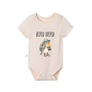May include: A light beige short-sleeve bodysuit featuring a graphic of a bird wearing a blue cap, a backpack, and hiking boots, with binoculars around its neck. The text BIRD NERD is printed in black above the illustration of the bird.