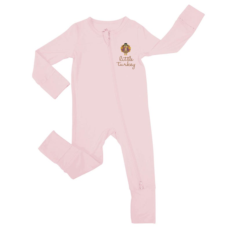 May include: A light pink baby sleeper with long sleeves and legs. The sleeper has a zipper down the front and a small graphic of a turkey wearing a hat with the words "little turkey" printed below it.