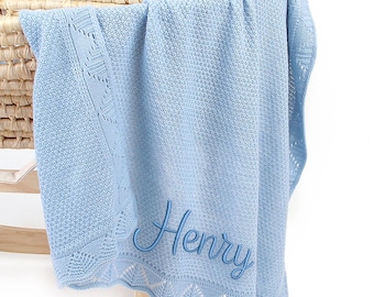 May include: A light blue knitted baby blanket with the name "Henry" embroidered in a matching blue script. The blanket has a decorative border with a scalloped edge and is draped over a wicker basket.