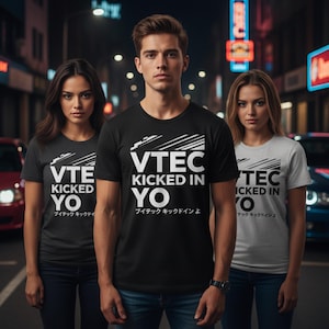 Könnte beinhalten: Drei Personen tragen T-Shirts mit dem weißen Text "VTEC KICKED IN YO". Die Shirts sind in Schwarz, Dunkelgrau und Hellgrau gehalten. Der japanische Text "ブイテック キックドインよ" steht darunter. Der Hintergrund ist eine nächtliche Stadtstraße.