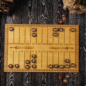 Peut inclure: Jeu de société en bois avec une bordure grecque, des chiffres romains et un motif d'épée. Le plateau comporte des emplacements pour des pions ronds avec des motifs de casques grecs. Le jeu est posé sur une surface en bois sombre.