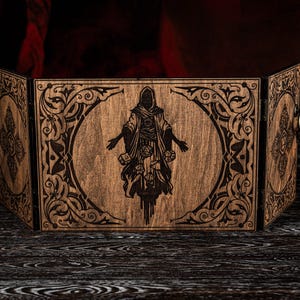 Puede incluir: Una pantalla de juego de mesa de madera con acabado en madera oscura. El panel central presenta una imagen grabada de una figura vestida con una túnica. Intricados diseños florales y de volutas bordean la imagen central y los paneles exteriores. Anillos metálicos en los paneles laterales.