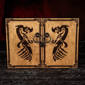 May include: A wooden box with two doors, featuring a dragon design carved into the wood. The box has a dark finish, metal ring handles, and decorative borders. The background is dark, highlighting the box's details.
