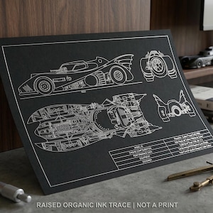 May include: Black blueprint-style print featuring detailed schematics of a Batmobile. The print includes multiple views and technical specifications, with the text "RAISED ORGANIC INK TRACE | NOT A PRINT" at the bottom. A digital caliper and a compass are in the foreground.