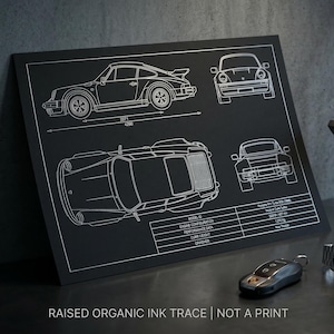 Puede incluir: Impresión en lienzo negro con un plano blanco de un Porsche 911 Turbo, con vistas laterales, superiores y frontales. Incluye especificaciones y el texto "RAISED ORGANIC INK TRACE | NOT A PRINT". Una llave de coche y un reloj están en primer plano.