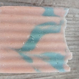 Puede incluir: Una pastilla de jabón con un patrón de remolino rosa y verde. El jabón tiene una superficie texturizada.