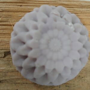 Puede incluir: Una pastilla de jabón redonda de color lavanda con un diseño floral decorativo.
