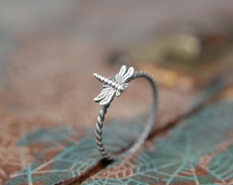 May include: A silver ring with a delicate dragonfly design. The ring is twisted and has a smooth finish.