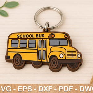 May include: A yellow school bus keychain with a brown wooden frame. The bus has the words "SCHOOL BUS" printed on the side. The keychain is attached to a silver key ring.