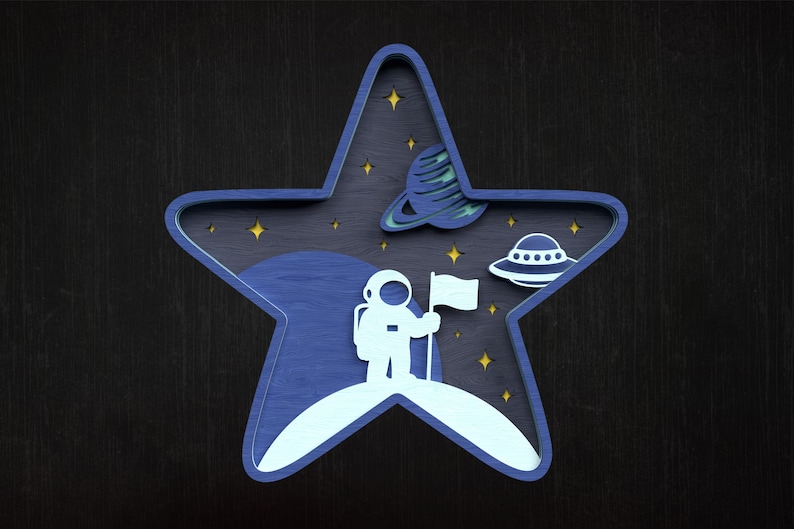 May include: A layered wooden star-shaped decoration with a space theme. It features an astronaut holding a flag on a planet, a planet with rings, and a UFO. The colour scheme includes shades of blue, white, and yellow.
