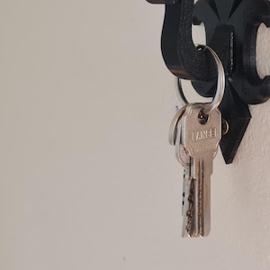 May include: Black metal wall hook with a decorative fleur-de-lis design. A set of keys is hanging on the hook.