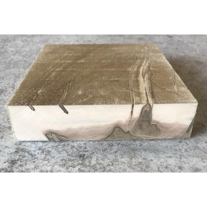 May include: A rectangular block of wood with a light brown top and a lighter, natural wood color on the sides. The wood grain is visible, with darker streaks and knots adding visual interest. The block appears to be freshly cut.
