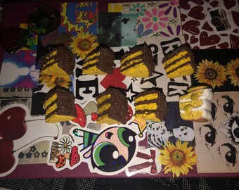 May include: A collection of nine miniature yellow and brown cakes with chocolate frosting. The cakes are arranged on a colourful background with various stickers and patterns.