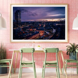 May include: A framed photograph of a city skyline at dusk. The photo shows a tall building in the foreground and a cityscape in the background. The sky is a mix of purple, pink, and orange.