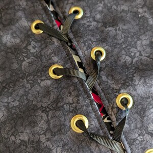 May include: Close-up of a black fabric with a floral pattern. The fabric has gold eyelets and black ribbon lacing.