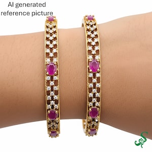 May include: Two gold-colored bangles with a repeating pattern of small white stones and larger oval-shaped red stones. The bangles are worn on a wrist, showcasing their design and color contrast. The jewelry is likely for fashion or special occasions.
