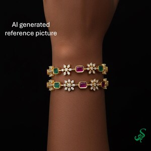 May include: Two gold bangles with emerald green and ruby red rectangular stones, interspersed with diamond-like flower accents. The bangles are displayed on a dark background. The text "AI generated reference picture" is visible.
