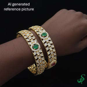 May include: Two gold-colored bangles with intricate designs and embedded gemstones. Each bangle features a central oval green stone, surrounded by smaller clear stones. The bangles are on a dark background.