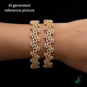 May include: Two gold-colored bangles with a floral design. Each bangle features a series of small, white, red, and green gemstones set in a repeating pattern. The bangles are displayed on a brown skin tone background.