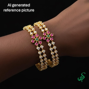 May include: Two gold bangles with a floral design, featuring white, pink, and green gemstones. The bangles are worn on a person's arm. The text "AI generated reference picture" is visible in the upper left corner.