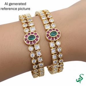 May include: Two gold-toned bangles with a repeating pattern of square and round clear stones. Each bangle features an oval centerpiece with a green stone surrounded by red stones. The bangles are worn on a wrist.