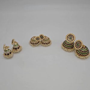 May include: Gold-toned, ornate earrings with intricate detailing. Each earring features a bell shape adorned with red, green, and clear gemstones, surrounded by a border of small pearls. The earrings are displayed on a white background.