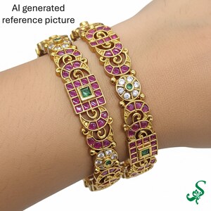 May include: Two gold bangles with intricate designs, featuring ruby-colored stones and emerald accents. The bangles are adorned with a series of circular and square patterns, creating a luxurious and ornate appearance. The text "AI generated reference picture" is visible.