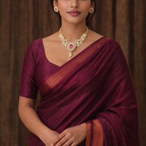 May include: A woman wearing a maroon sari with a gold and gemstone necklace and matching earrings. The sari has a gold border. The image has the text "AI generated reference picture" at the bottom.