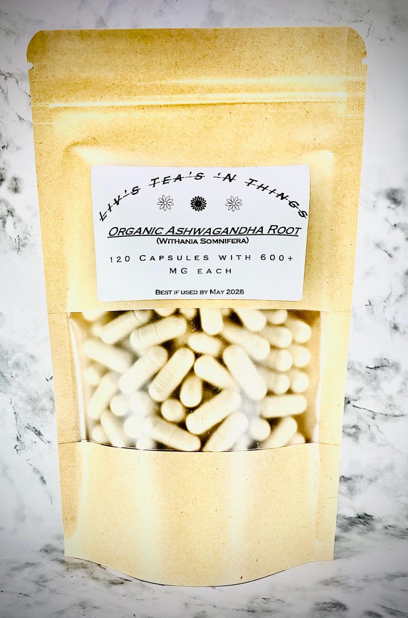 May include: A tan pouch with a clear window showing many white capsules. The pouch has a white label with the text "Liv's Tea's 'N Things" and "Organic Ashwagandha Root" with details about the capsules, including the quantity and milligrams.